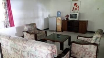 A living room with patterned sofas, a small table, a water dispenser, and a television on a wooden cabinet.