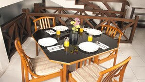 Una mesa de comedor dispuesta para cuatro personas, con sillas de madera, un jarrón con flores y vasos de jugo de naranja.