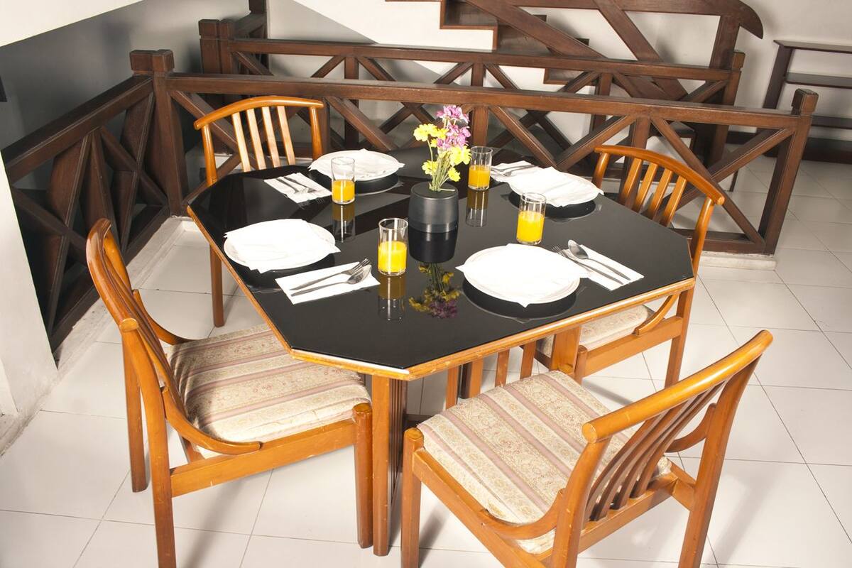 A dining table set for four with wooden chairs, a vase with flowers, and glasses of orange juice.