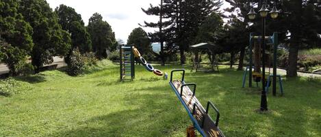 Un parque con un arenero, una estructura para escalar y columpios en un área verde.