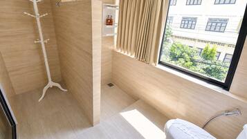A modern bathroom with a shower, a toilet, and a window with a view of buildings and greenery.