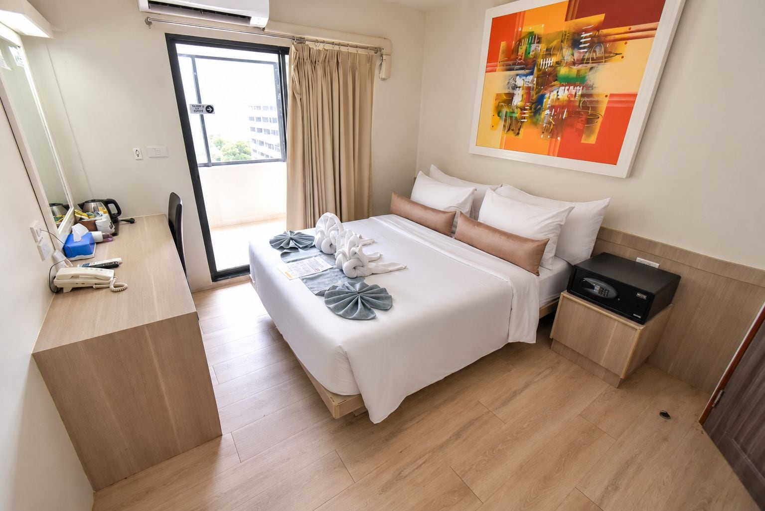 A hotel room with a bed, a desk, a telephone, and a painting on the wall.