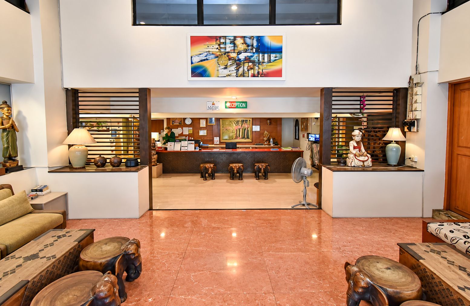 A hotel lobby with a reception desk, a receptionist, and a reception sign. There are decorative stools and a statue on the left side.
