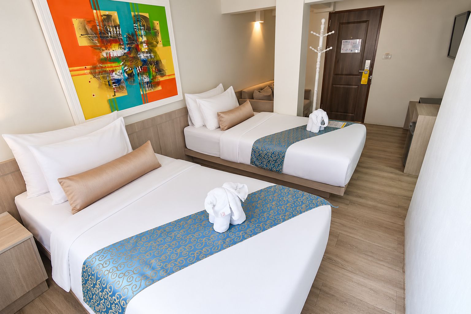 Habitación de hotel con dos camas, un cuadro en la pared y un perchero.