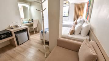 A hotel room with a bed, a sofa, a desk with a computer, a telephone, and a small refrigerator.