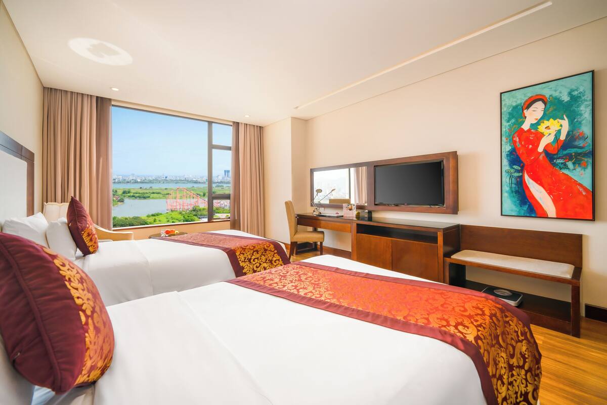 A hotel room with two beds, a desk, a television, and a painting.