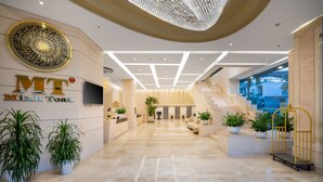 A modern hotel lobby with a reception desk, potted plants, a staircase, and a large chandelier. - Minh Toan Galaxy Hotel (Da Nang)