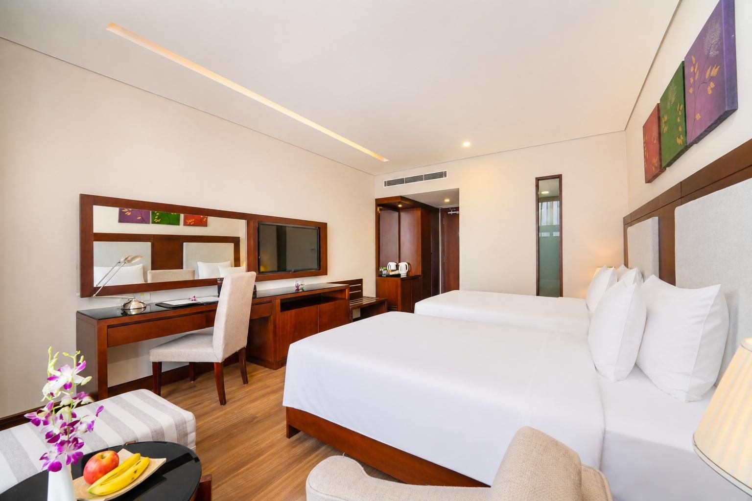 Habitación de hotel con cama, escritorio, silla y una pequeña mesa con fruta.