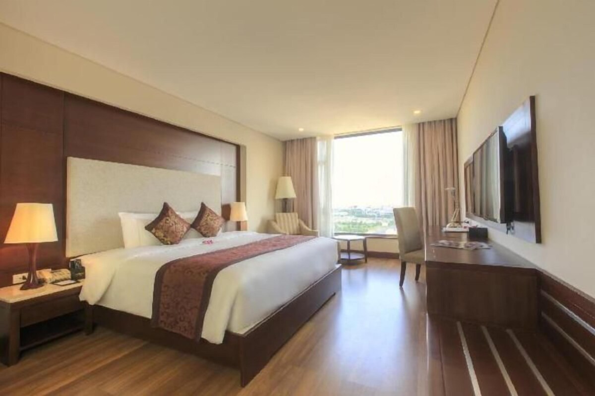 A hotel room with a large bed, a desk, a chair, and a TV mounted on the wall.