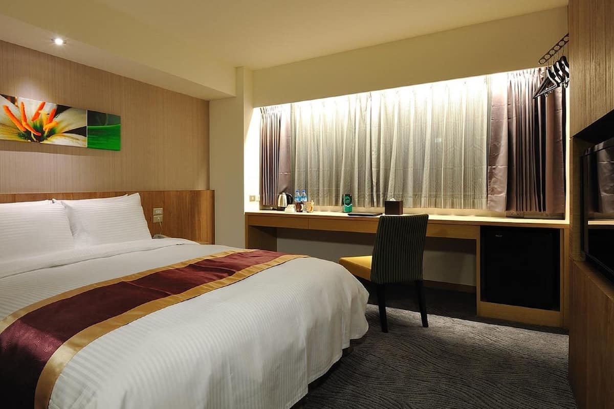 A hotel room with a large bed, a desk, a chair, a TV, and a window with curtains.