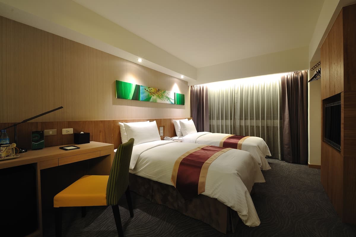 A hotel room with two beds, a desk, a chair, and a TV.