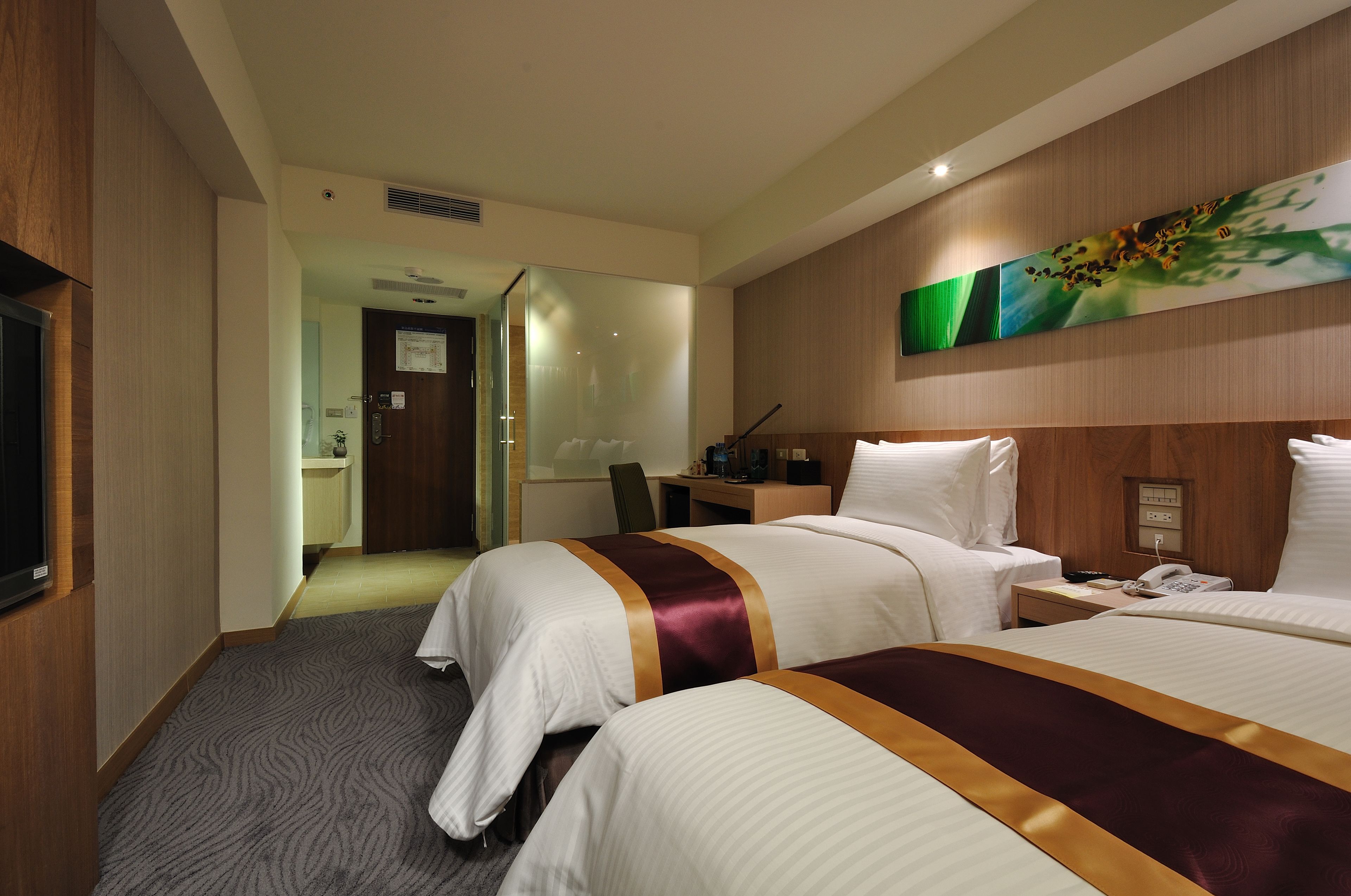 Habitación de hotel con dos camas, un escritorio, una silla, un televisor y un cuadro en la pared.