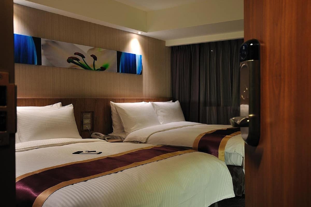 A hotel room with two beds, a wooden headboard, a painting above the beds, a telephone, and a door with a handle.