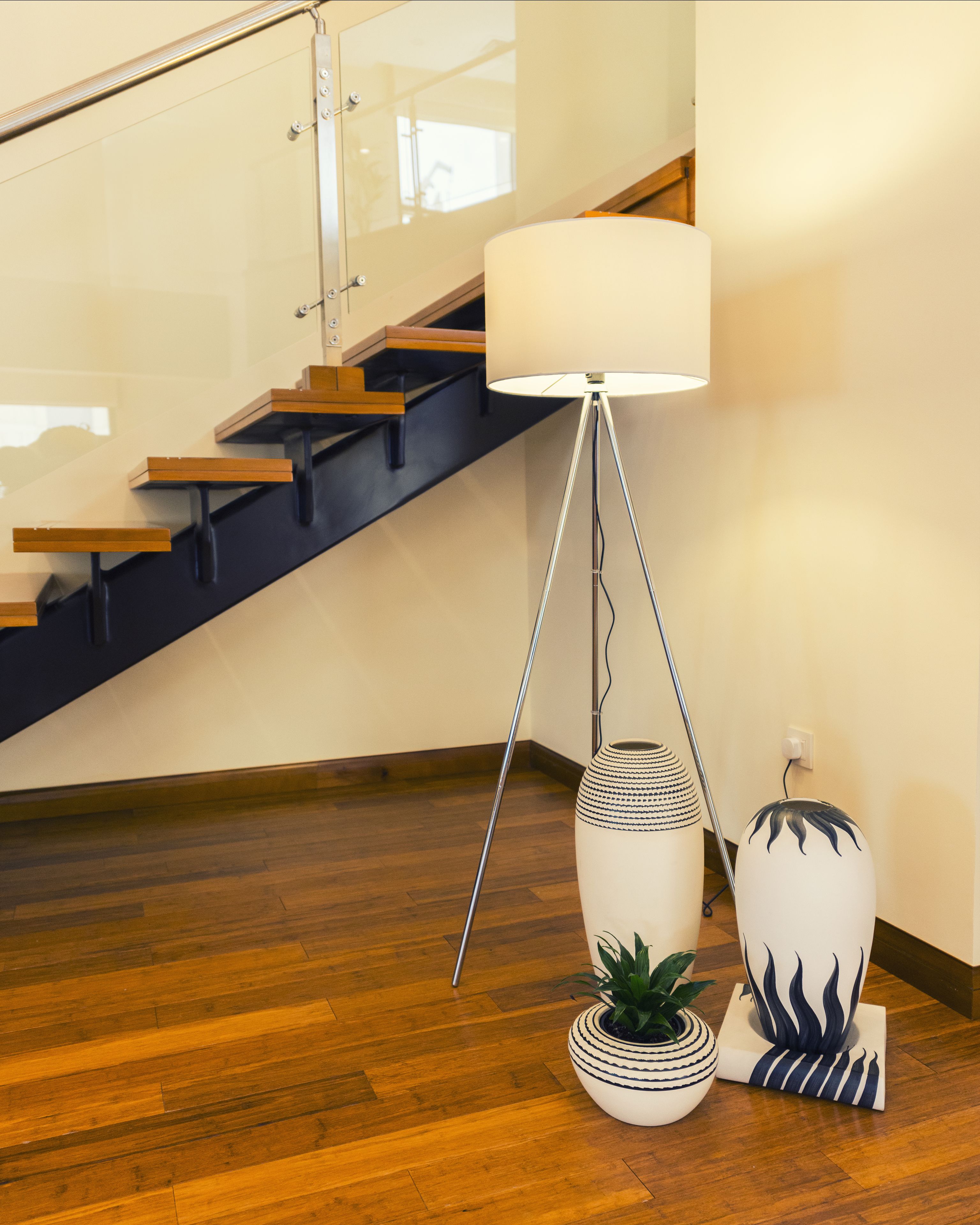 A modern interior with a wooden staircase, a floor lamp, and two decorative vases.