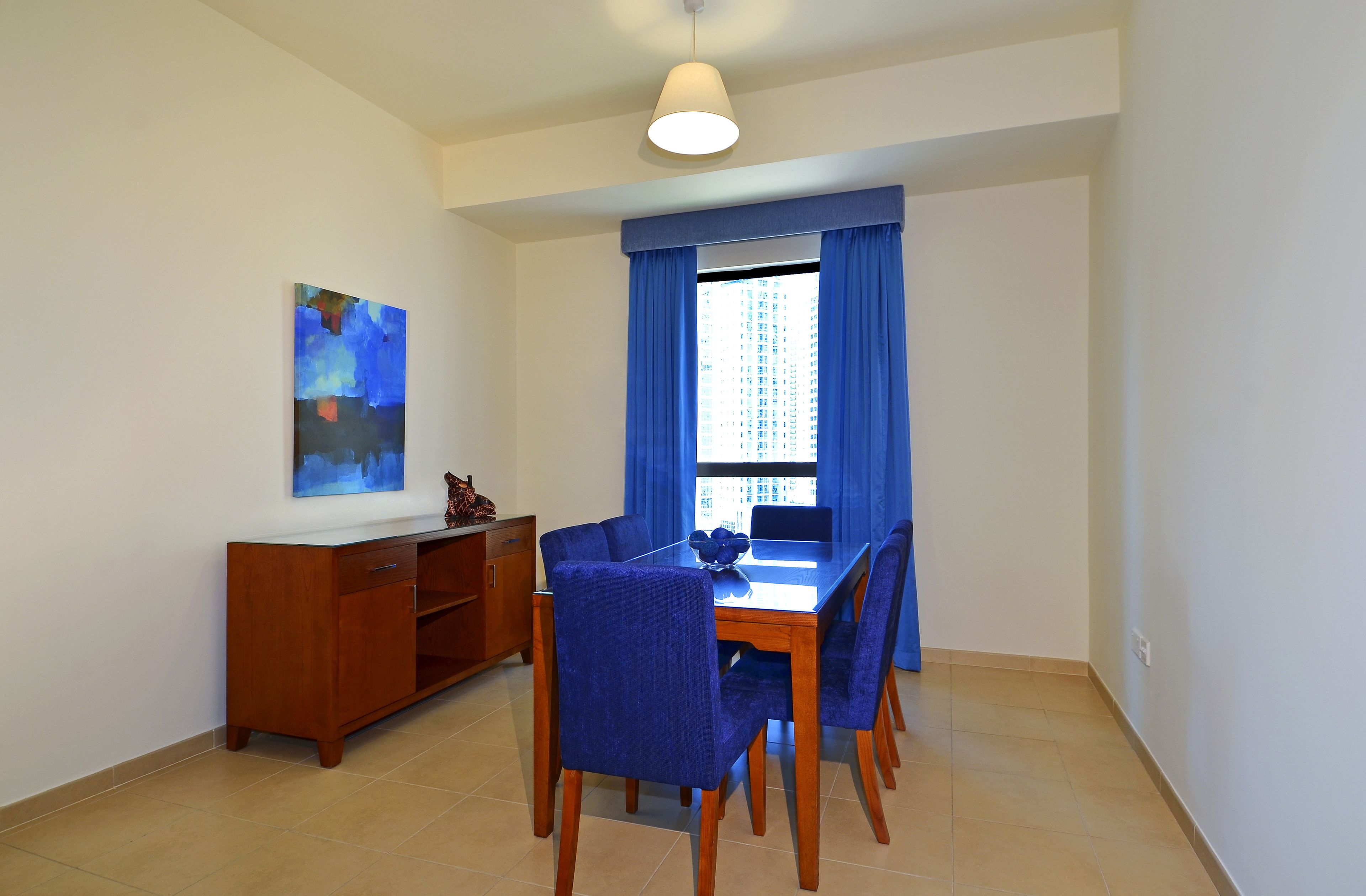 A dining area with a wooden table and blue upholstered chairs, a wooden cabinet, and a blue curtain.