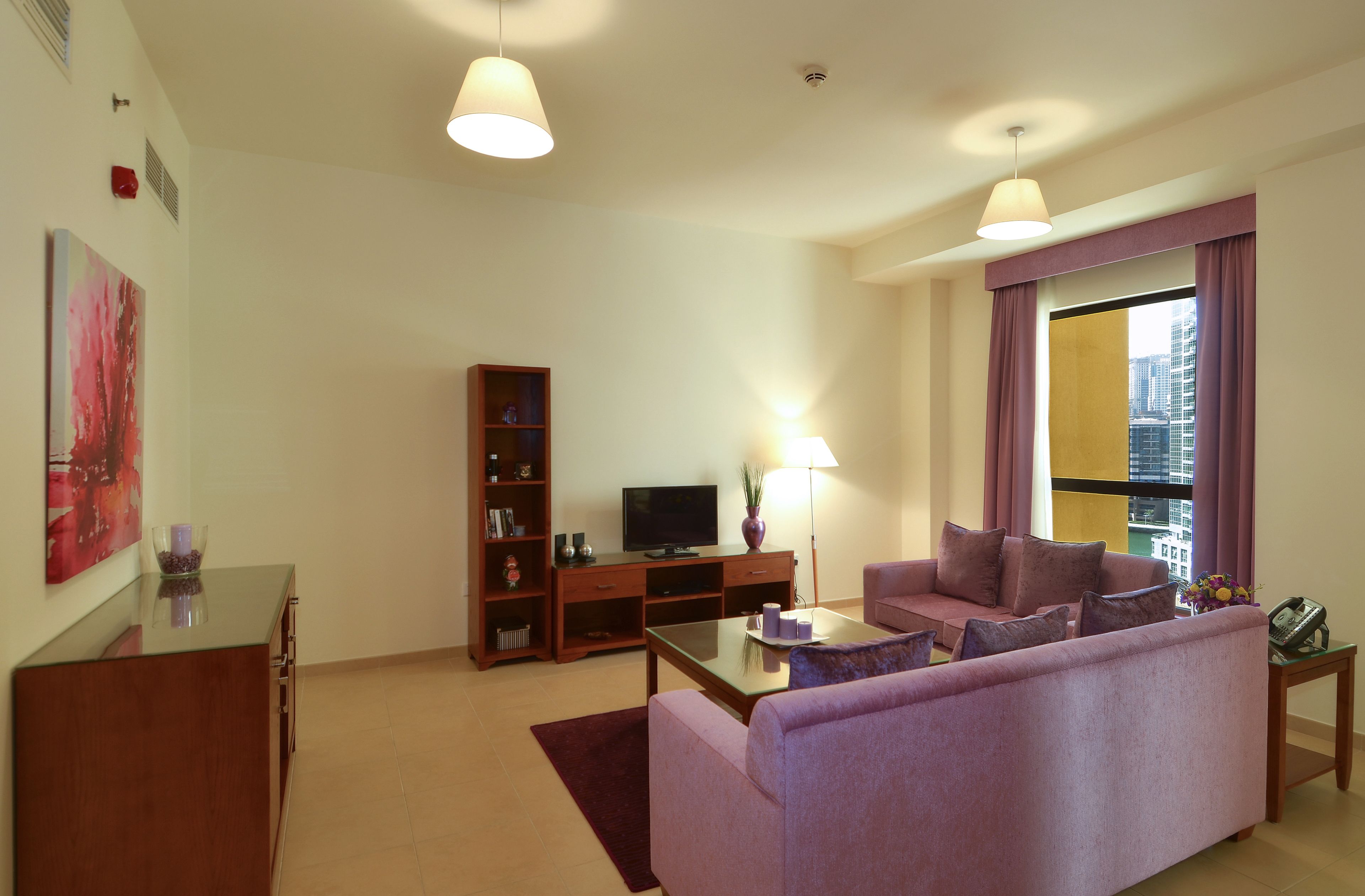 Una sala de estar con un sofá, un televisor, una estantería y un ventanal con cortinas.