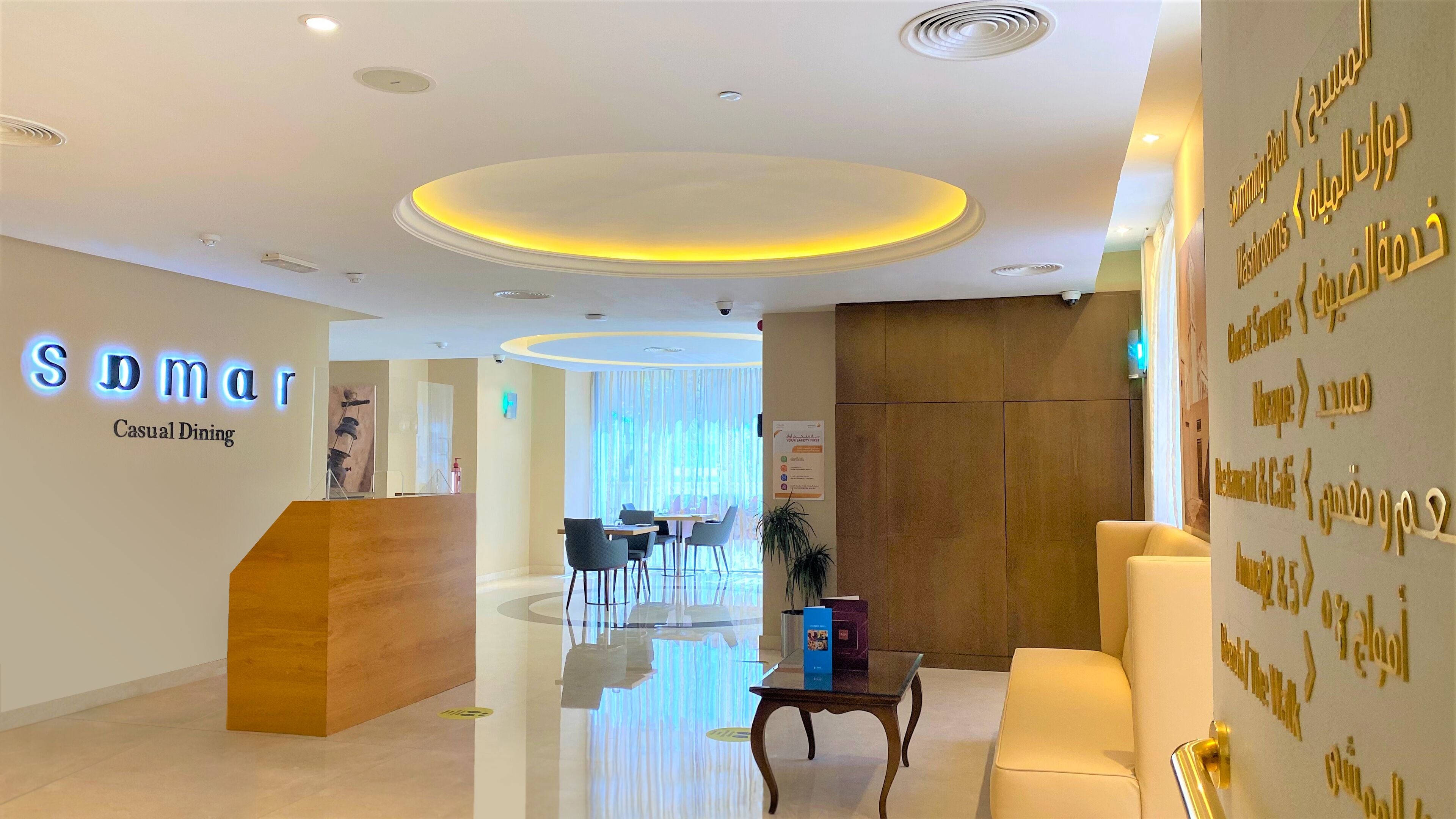 A hotel reception area with a modern design, including a reception desk, seating area, and a wall with directional signs.