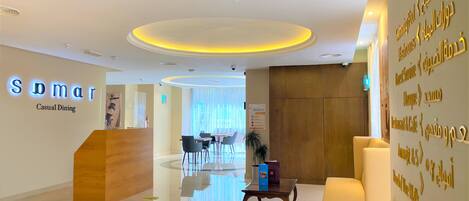 A hotel reception area with a modern design, including a reception desk, seating area, and a wall with directional signs.