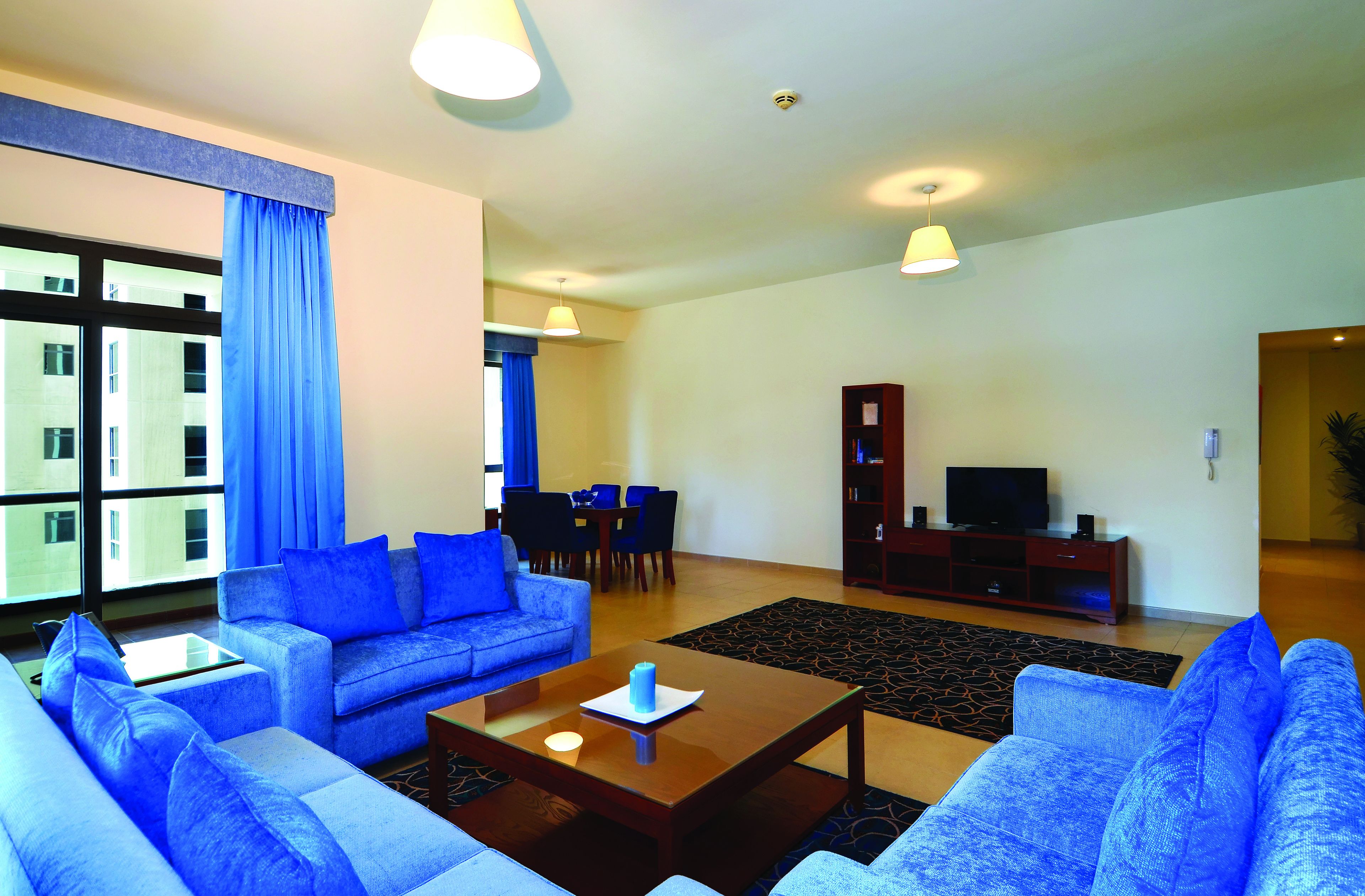 Ein modernes Wohnzimmer mit einer blauen Sofagarnitur, einem Couchtisch und einem Fernseher auf einem Holzgestell.