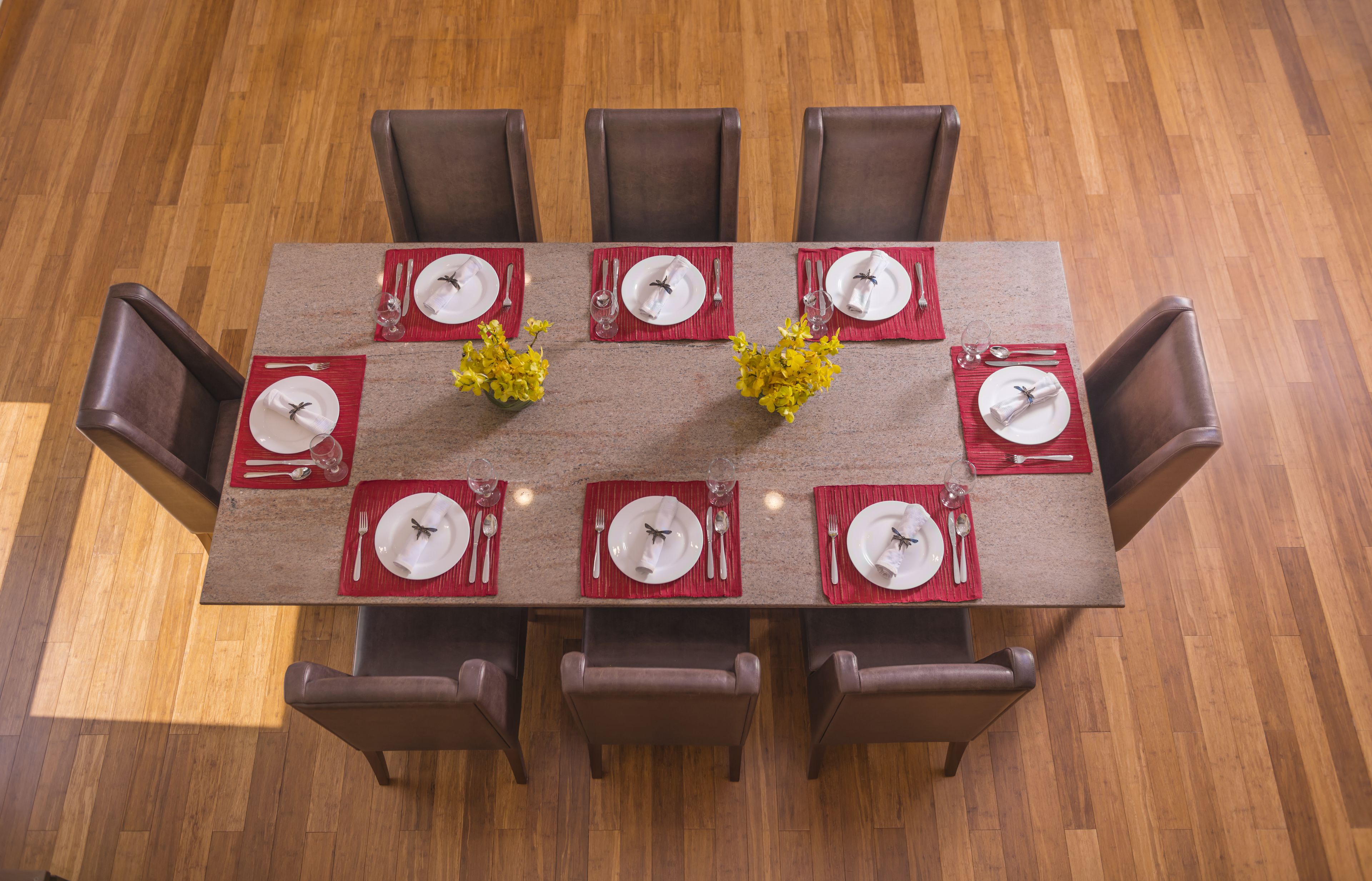 A rectangular dining table with six chairs, each with a red placemat and white plates.