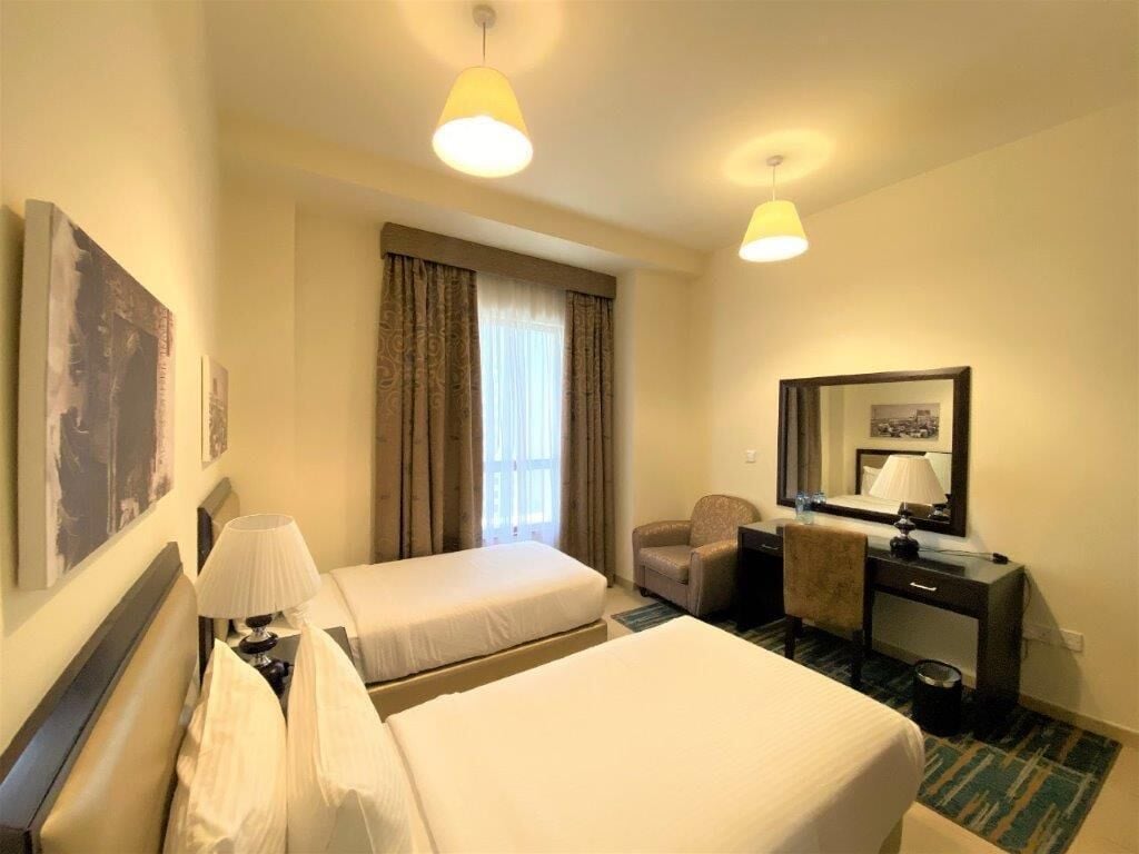 Een hotelkamer met twee bedden, een bureau, een stoel, een spiegel en een raam met gordijnen.