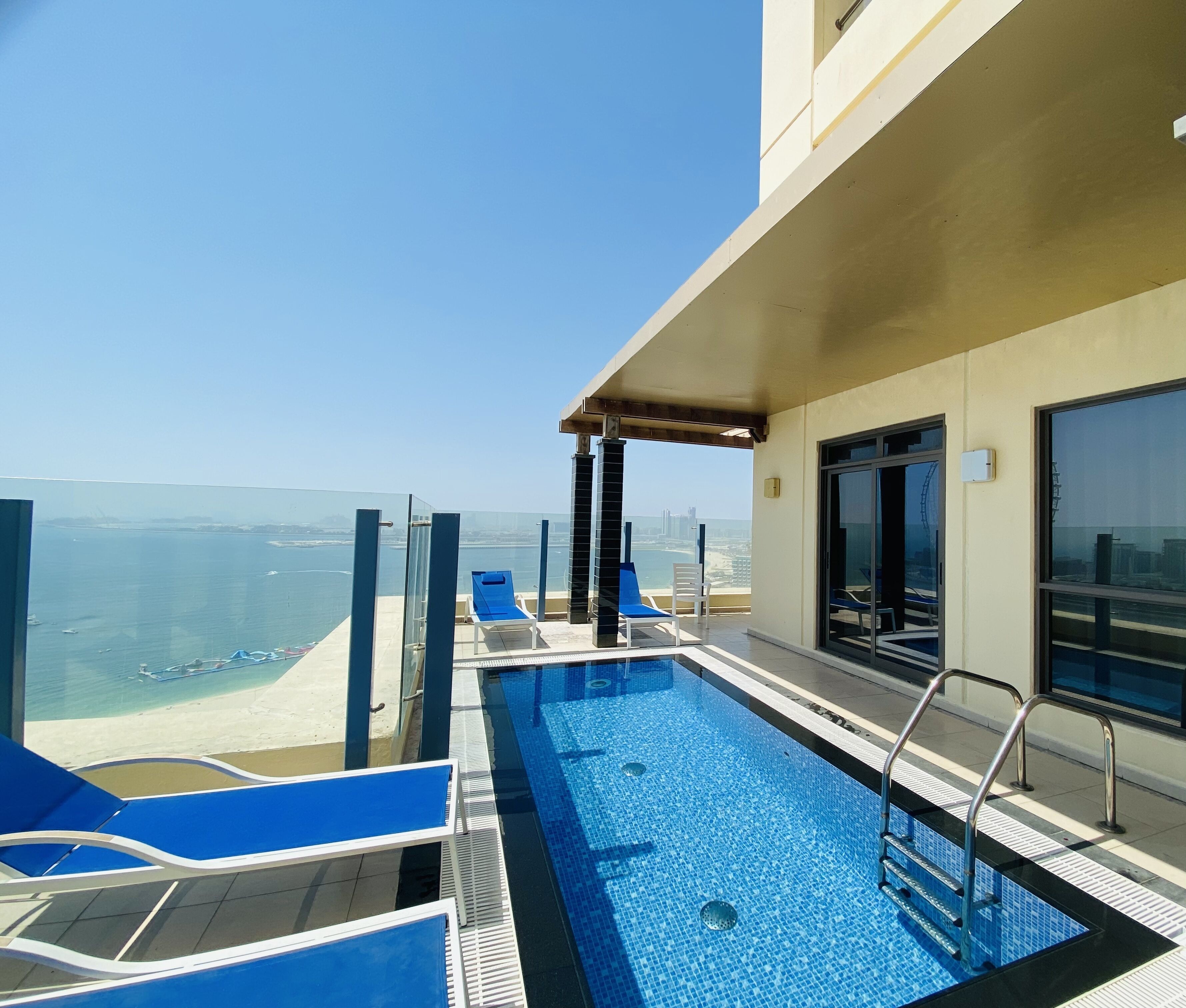 A rooftop pool with blue lounge chairs and a view of the sea.