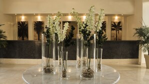 A lobby with a marble reception desk, clear glass vases with white flowers and pebbles, and various artworks on the walls. - JAZ Neo Naama Bay (Sharm El Sheikh)