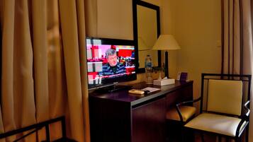 A hotel room with a television, a desk, a chair, a lamp, and curtains.