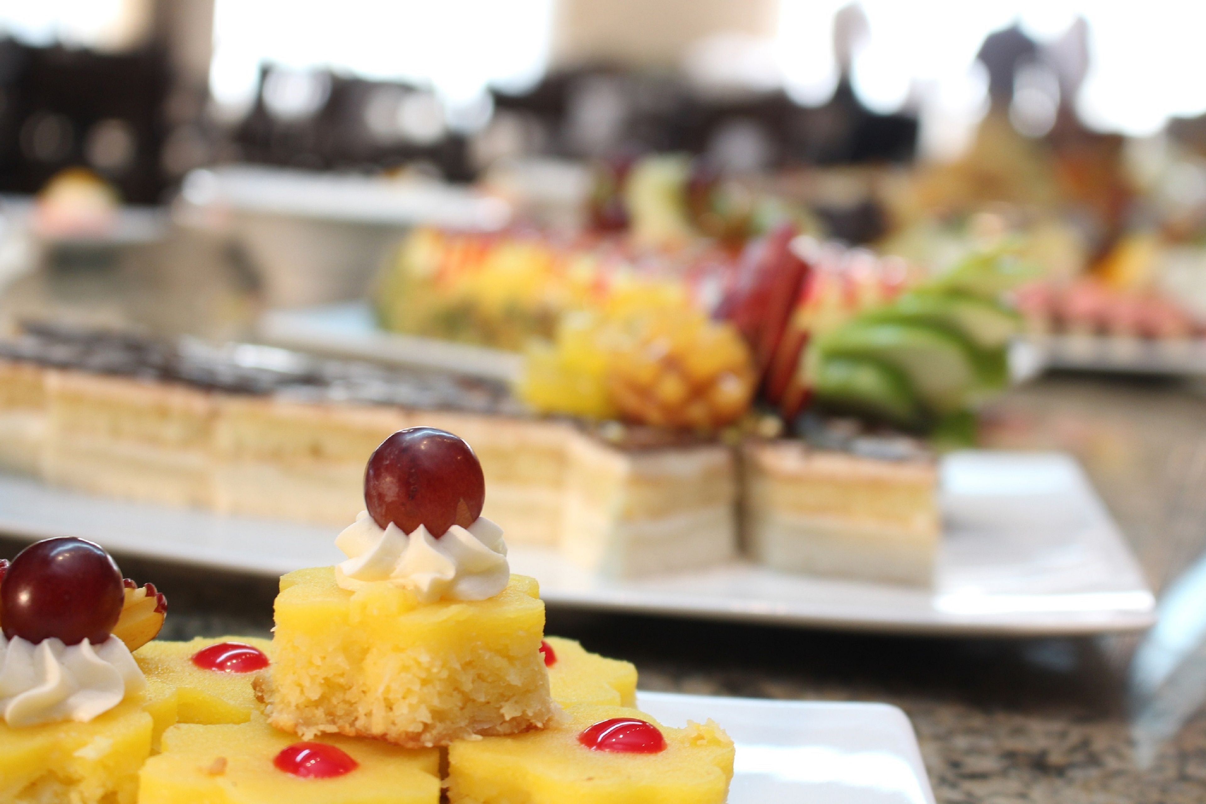 Eine Auswahl an Desserts auf einem Buffet, darunter ein Stück gelber Kuchen mit Kirschen und Schlagsahne.