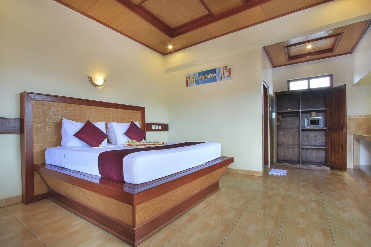 A large bed with a wooden frame and white bedding, a wall-mounted light, and a wooden cabinet with a microwave.