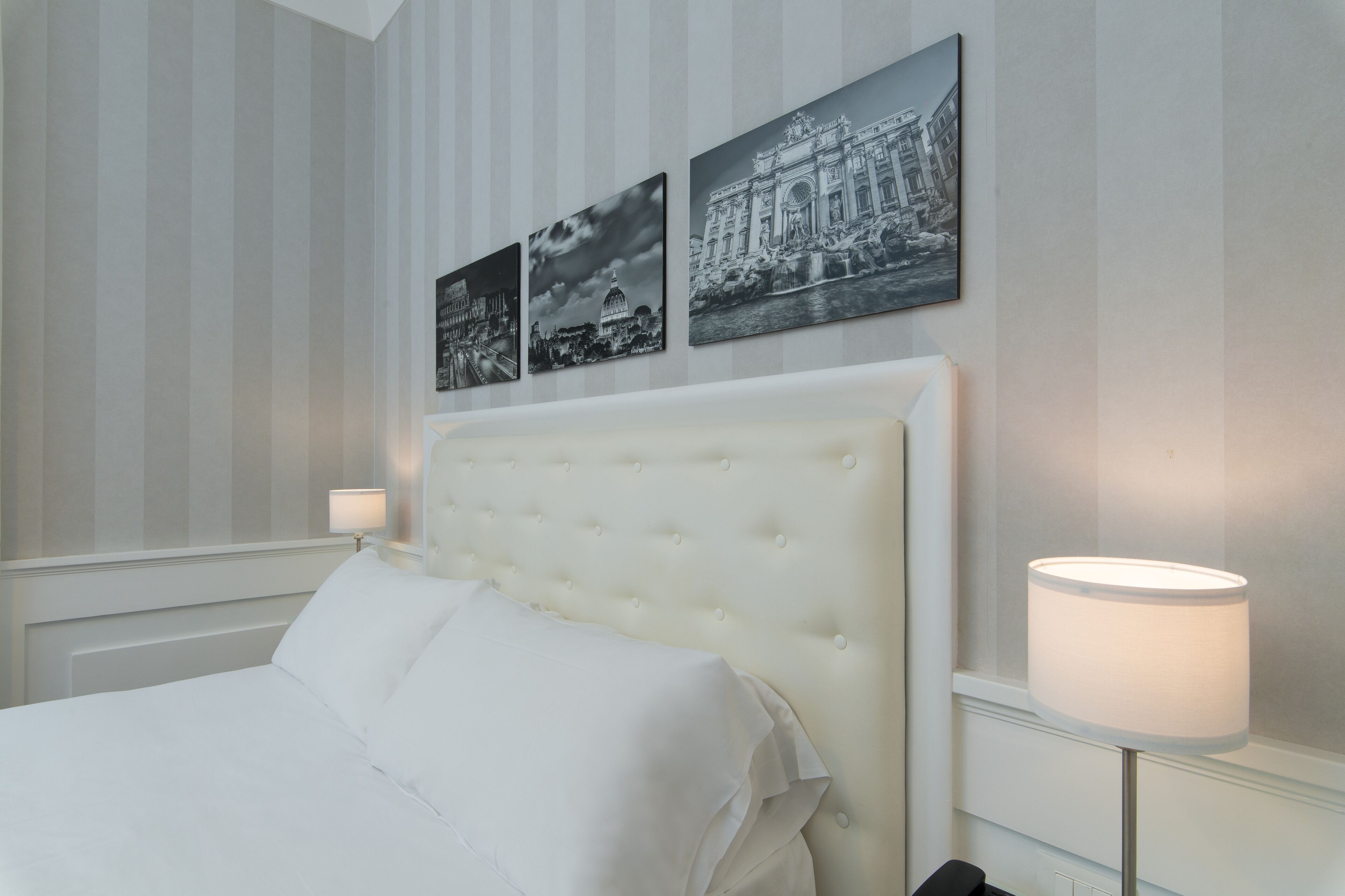 A neatly made bed with a tufted headboard, a bedside lamp, and three black-and-white photographs on the wall.