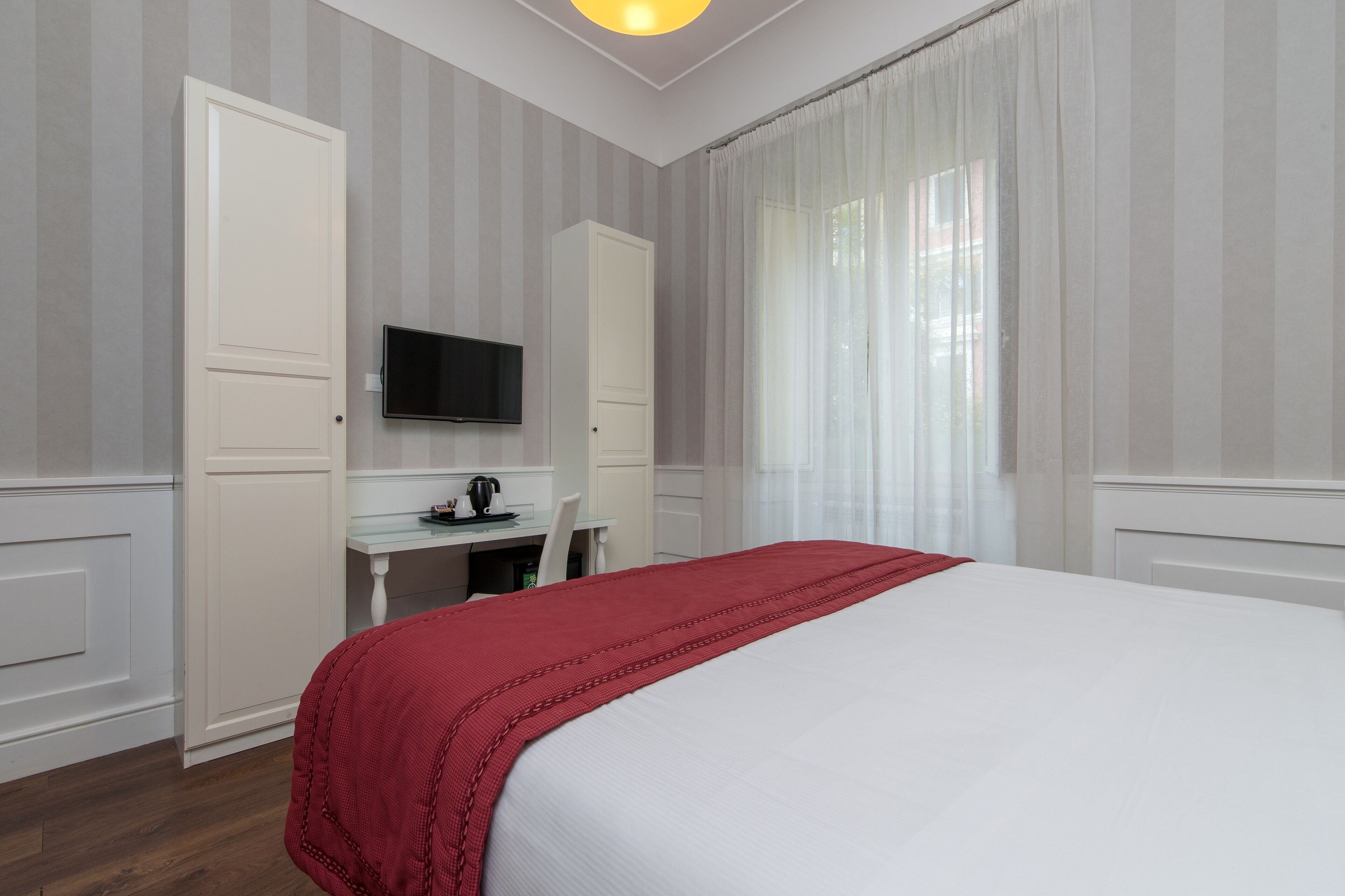 Una habitación de hotel con cama, escritorio, televisor y ventana con cortinas.