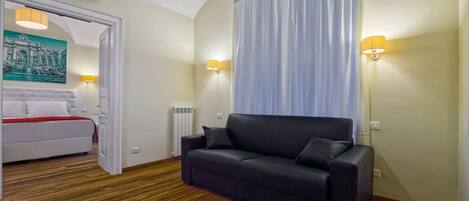 Une chambre d’hôtel avec un lit, un canapé en cuir noir, un plancher en bois, un radiateur et deux lampes fixées au mur.