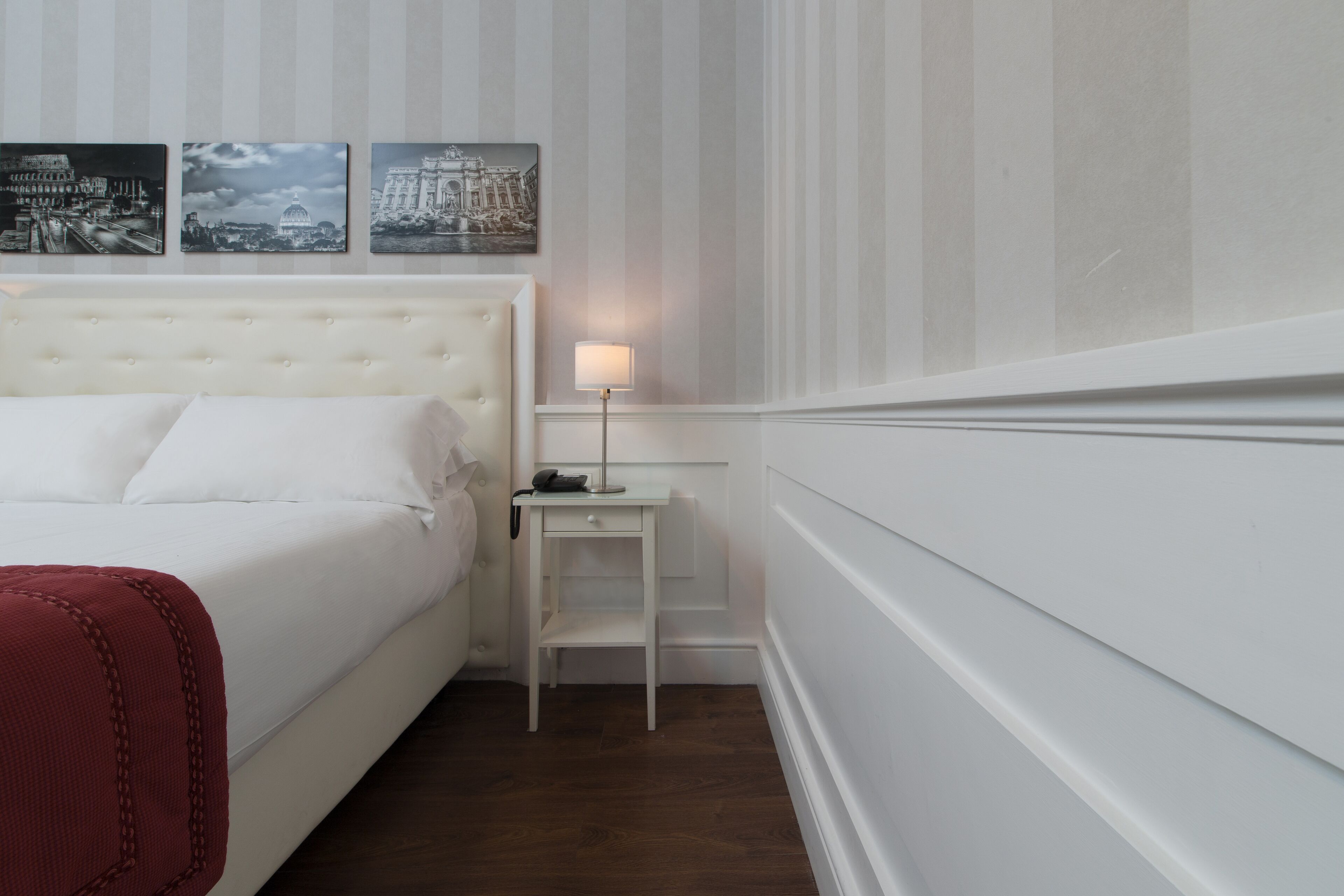 A hotel room with a large bed, a nightstand with a lamp, and three cityscape pictures on the wall.