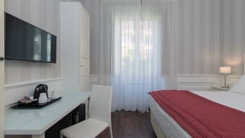 A hotel room with a bed, a desk with a coffee maker, a chair, a TV, and a window with curtains.