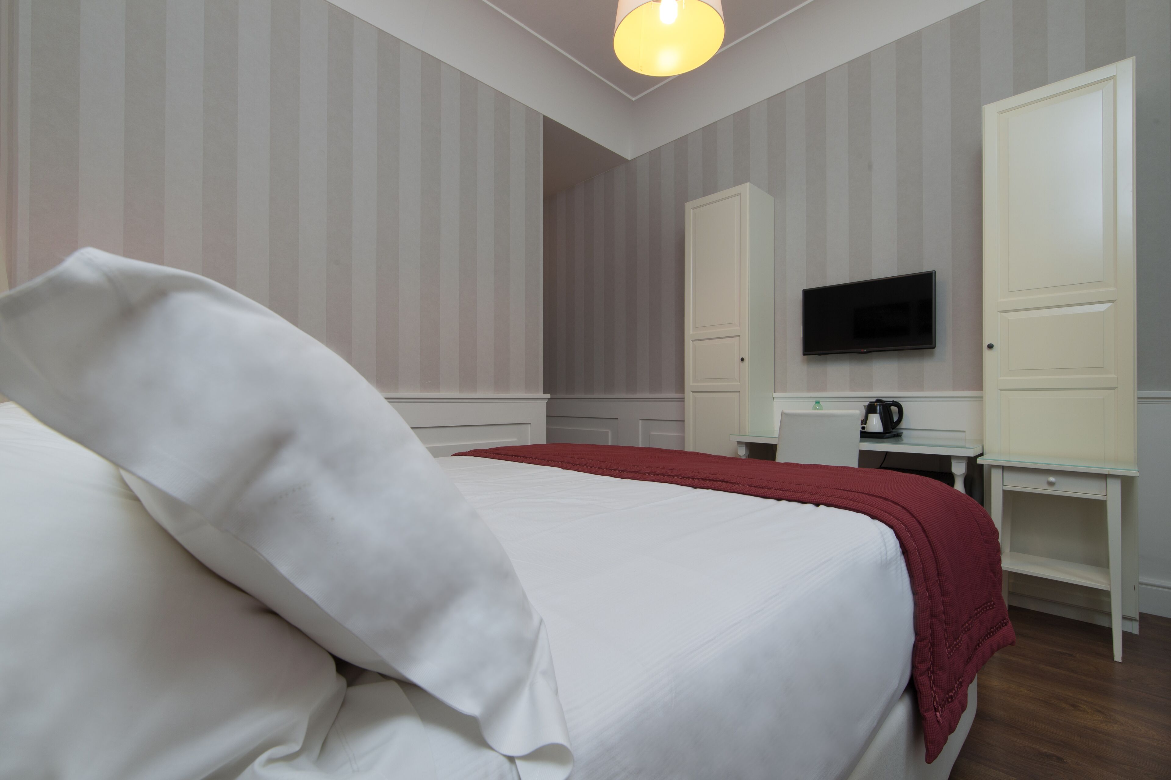 A hotel room with a bed, a desk, a television, and a wardrobe.