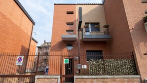 Un edificio de varios pisos con fachada de ladrillo, entrada con portón y un pequeño balcón con plantas en macetas.
