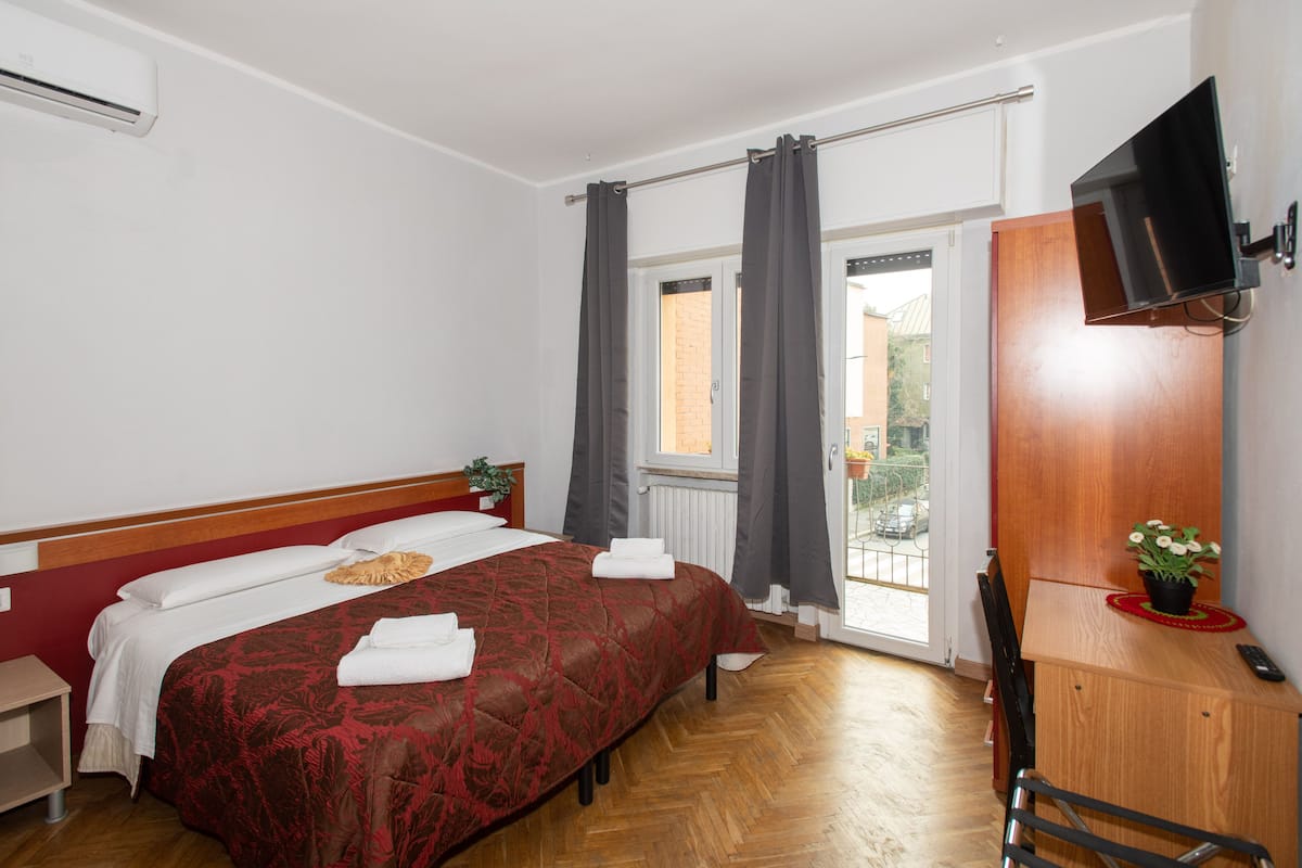 A hotel room with a bed, a desk, a chair, a TV, and a window with curtains.