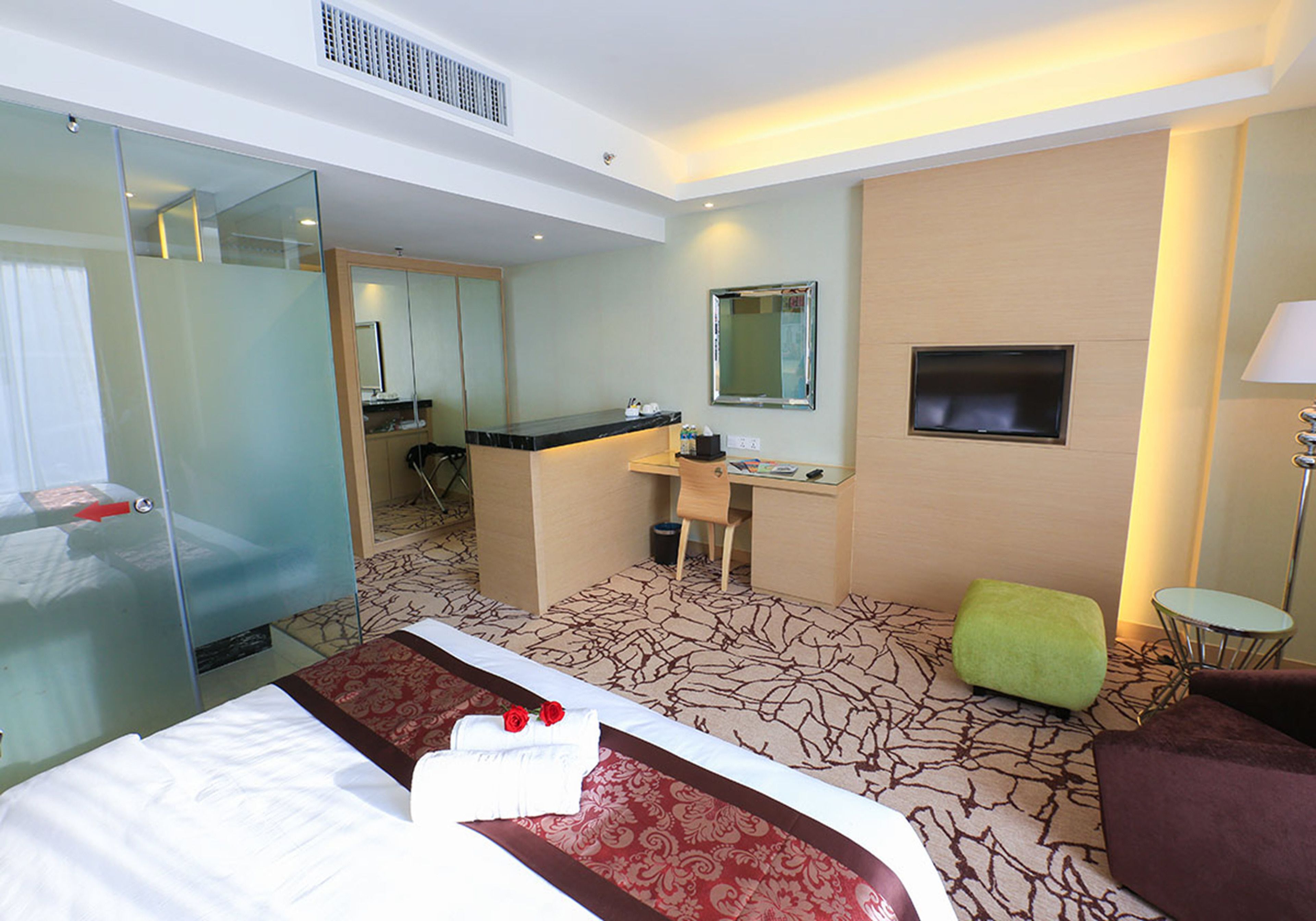 Una habitación de hotel con cama, escritorio, espejo, televisor y una pequeña mesa redonda.