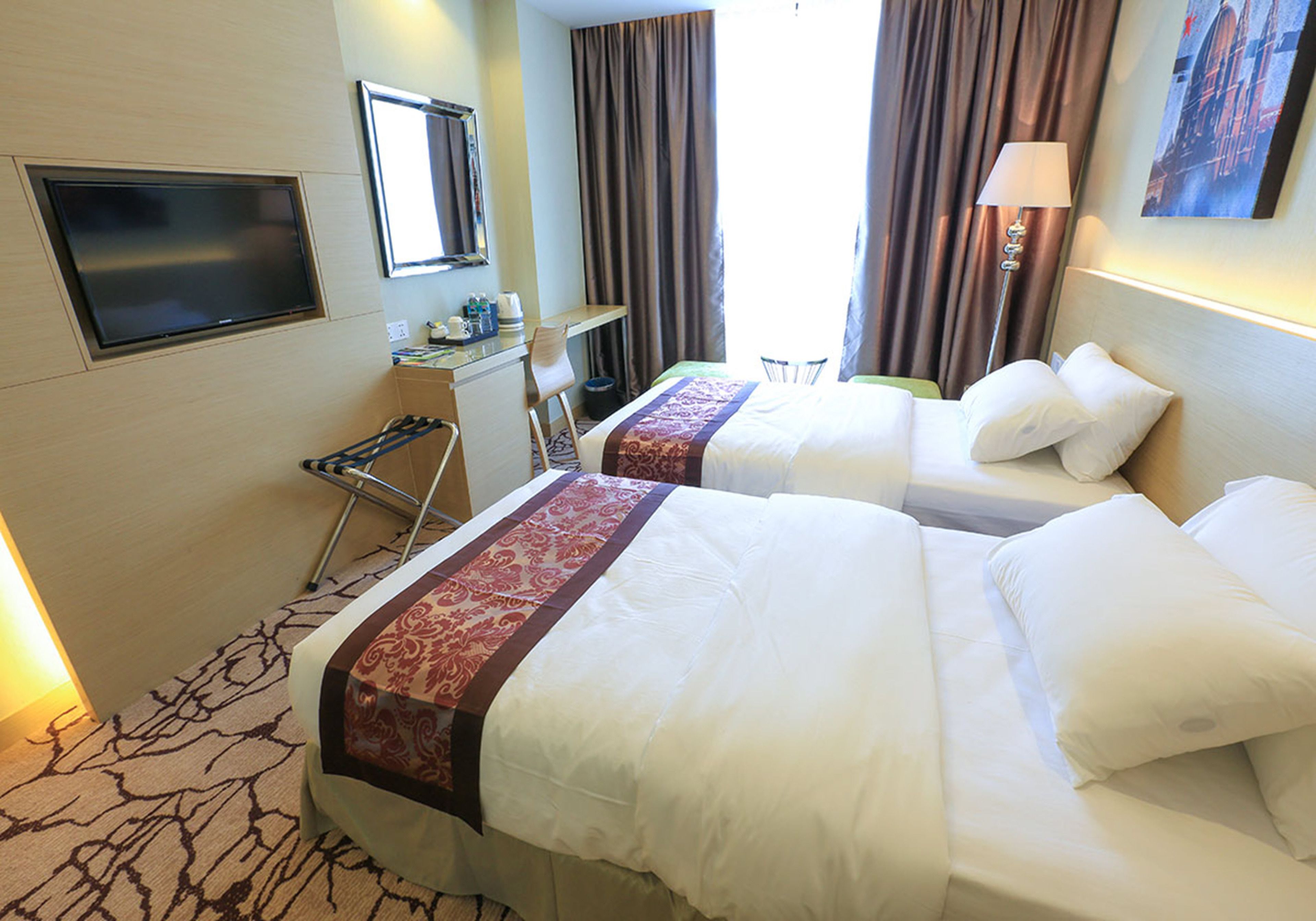 A hotel room with two beds, a desk, a chair, a TV, and a lamp.