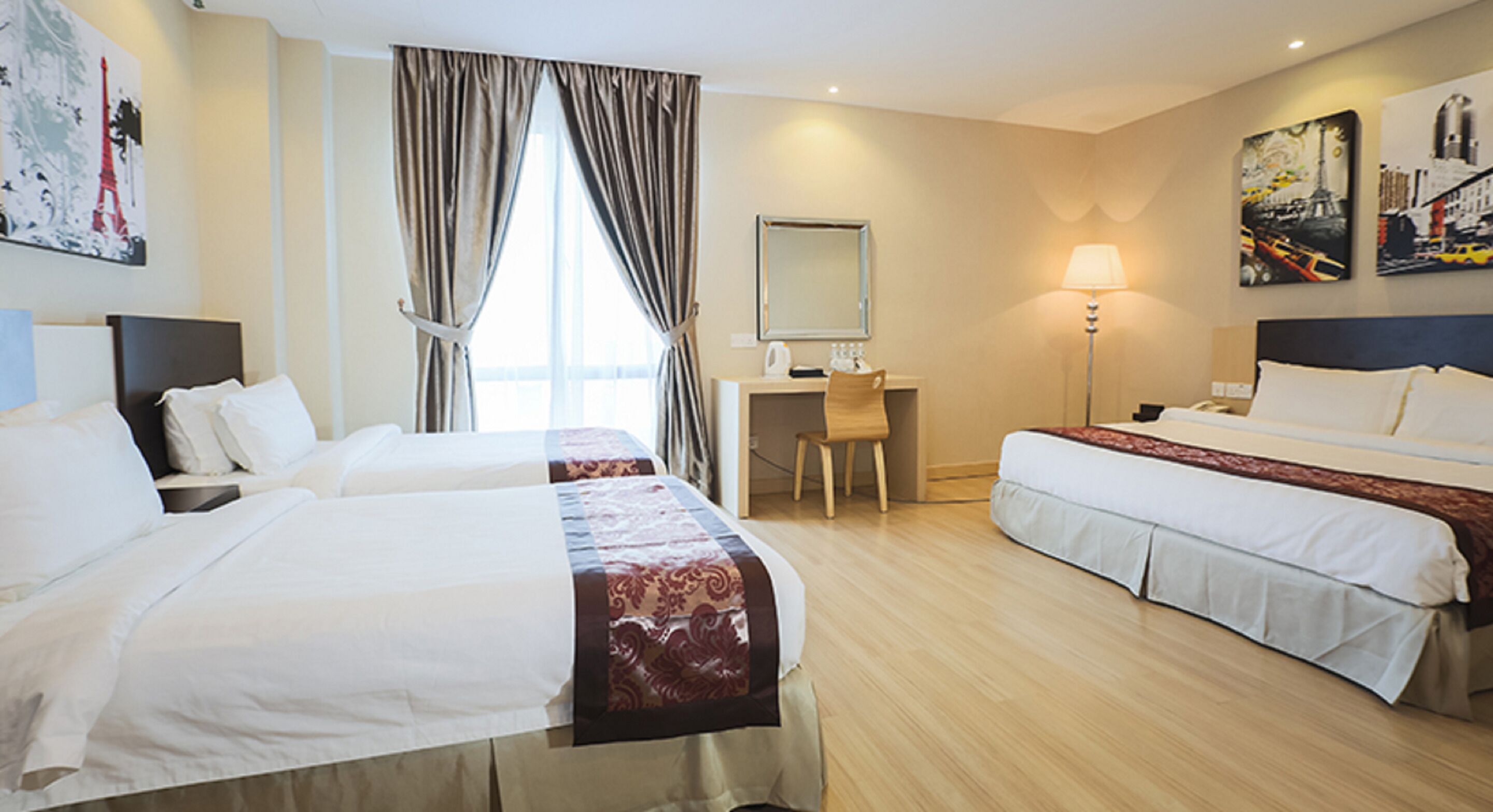 Une chambre d’hôtel avec deux lits, un bureau, une chaise, une lampe et des œuvres d’art accrochées aux murs.