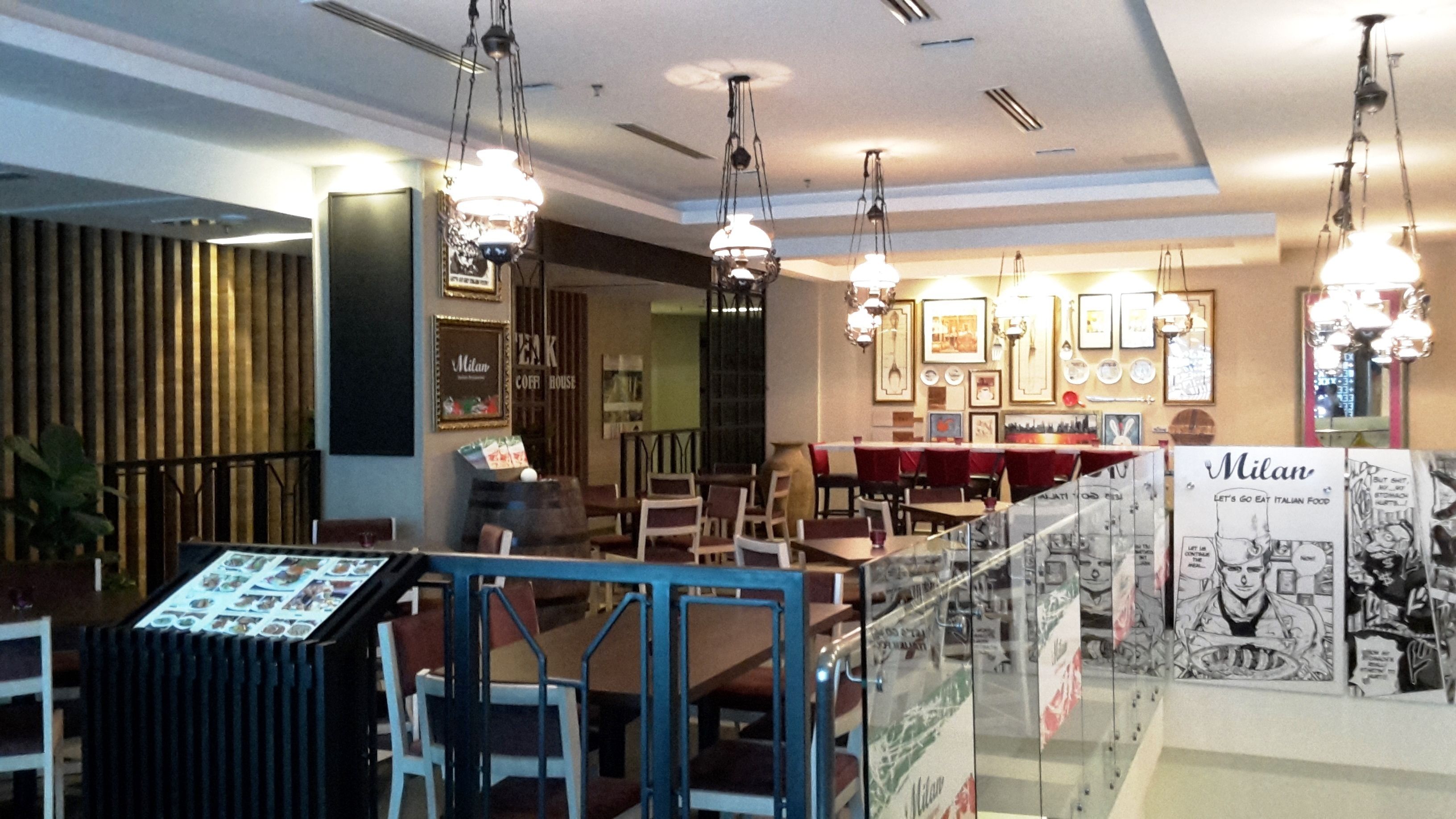 Interior de un restaurante con luces colgantes, cuadros en las paredes y una vitrina con el menú.