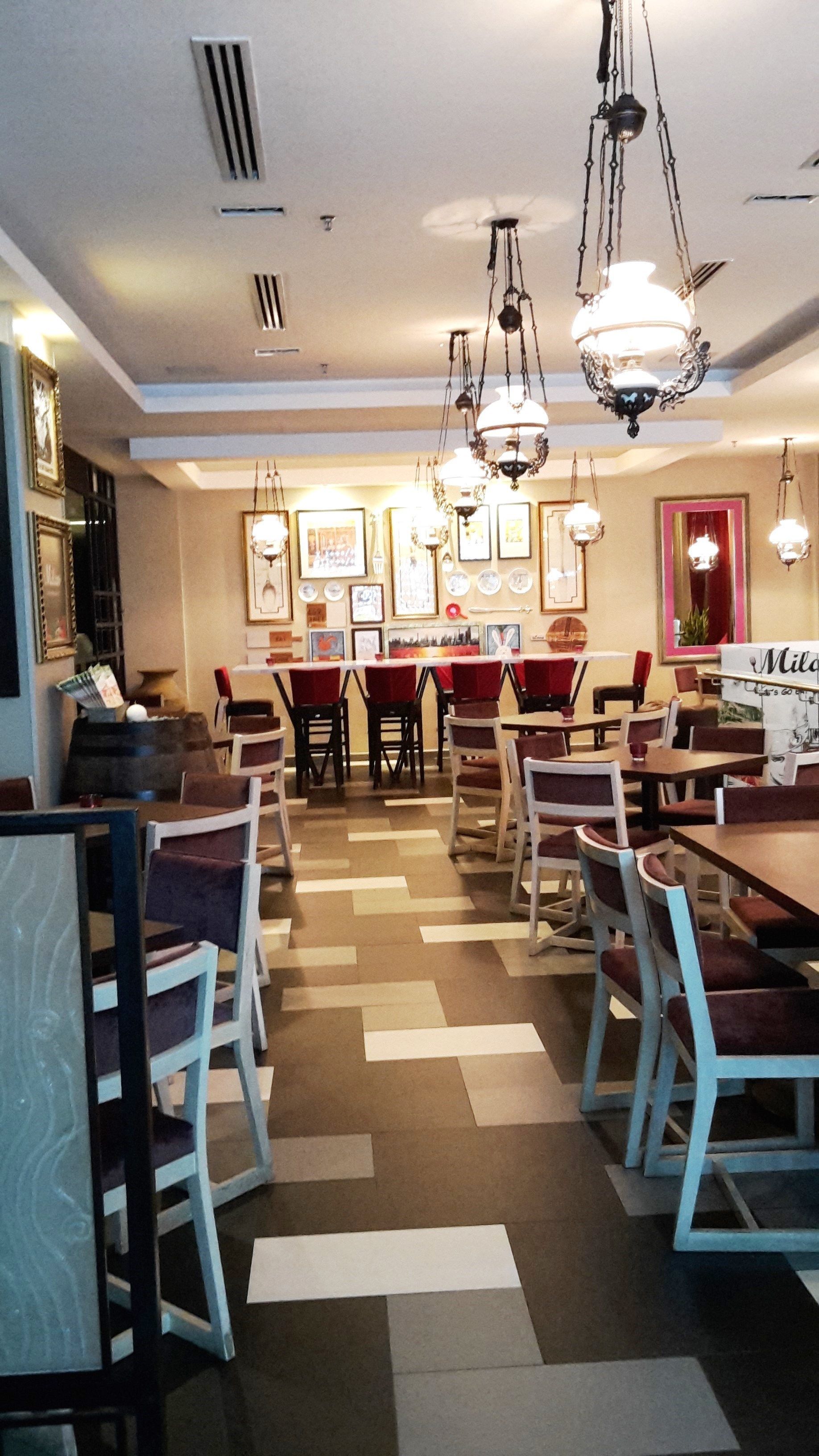 A restaurant interior with multiple tables and chairs, decorative lighting, and framed pictures on the walls.