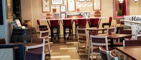 A restaurant interior with multiple tables and chairs, decorative lighting, and framed pictures on the walls.