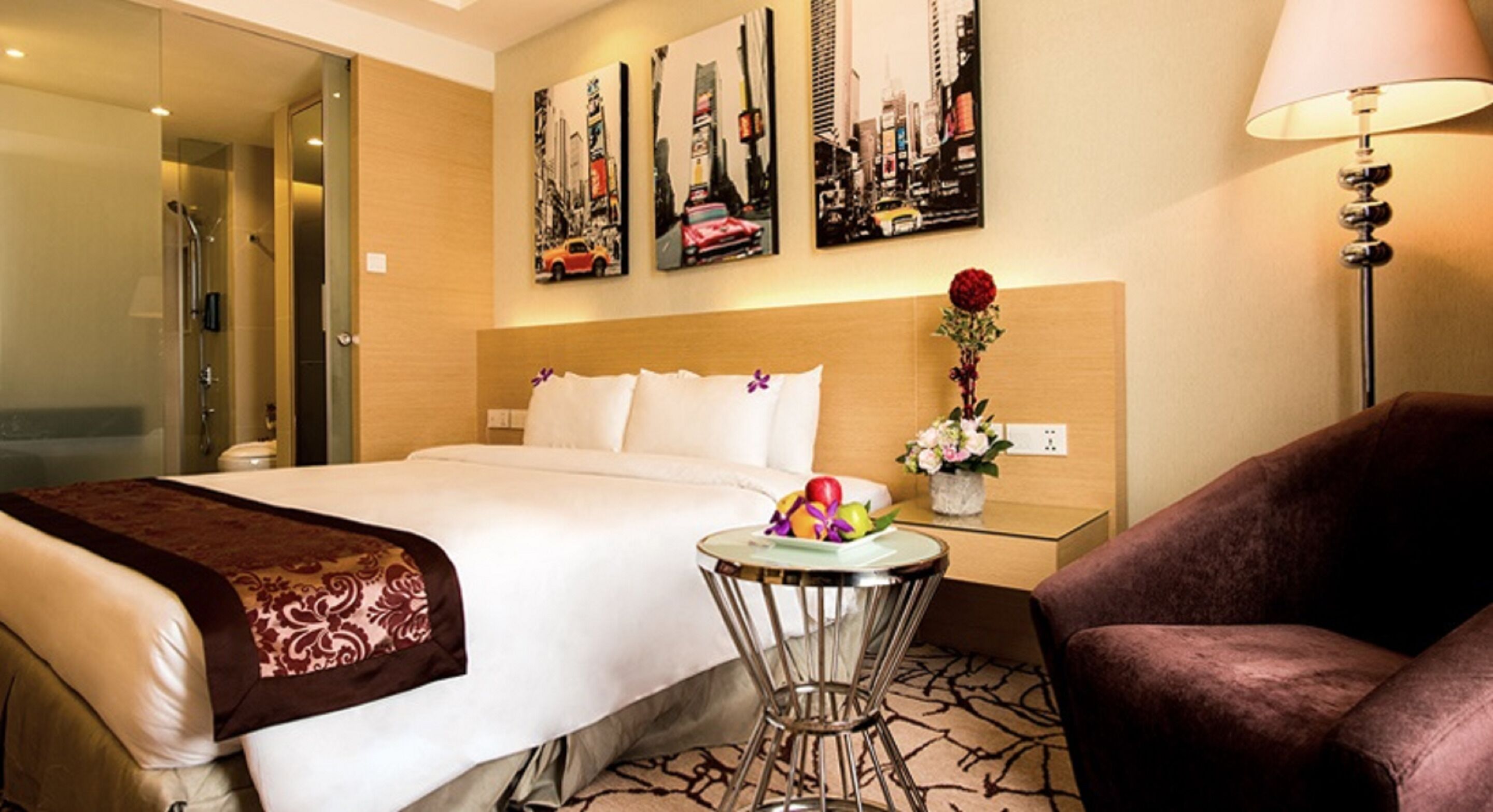 Una habitació d'hotel amb un llit, una taula de nit amb un ram de flors, una cadira i una làmpada.