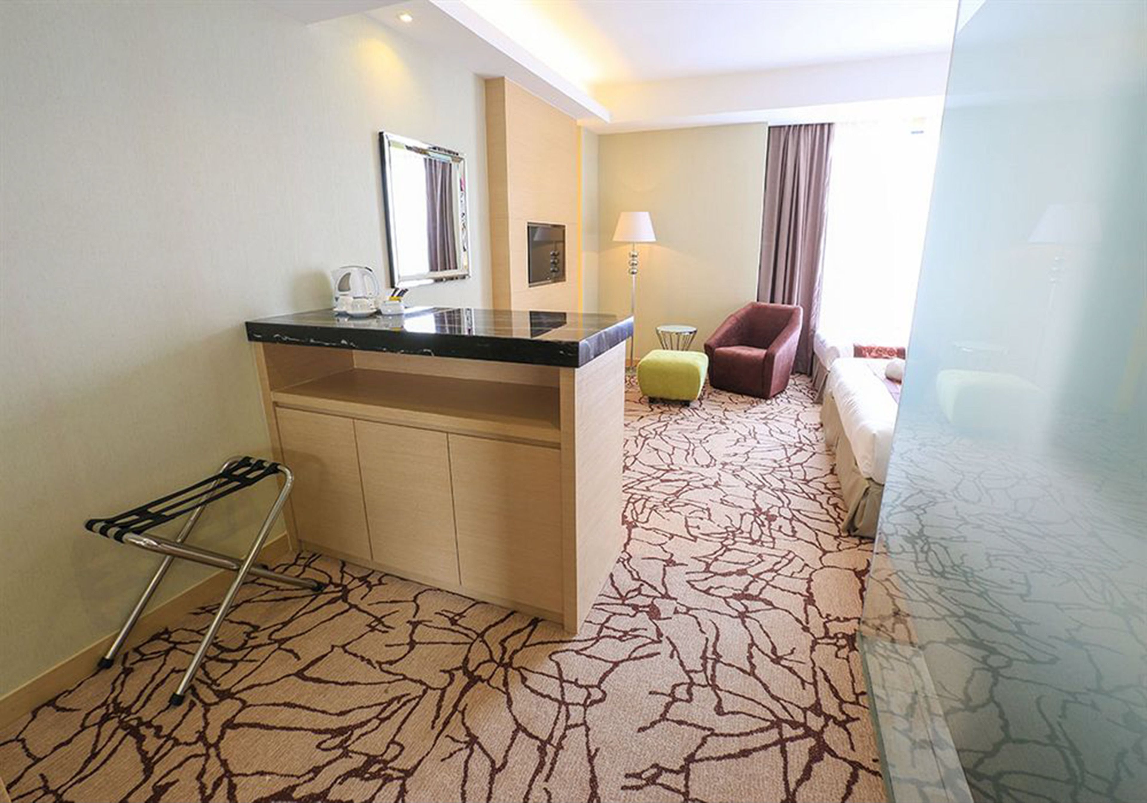 Une chambre d’hôtel équipée d’une kitchenette, d’un petit coin salon, d’un lit et d’une moquette à motifs.