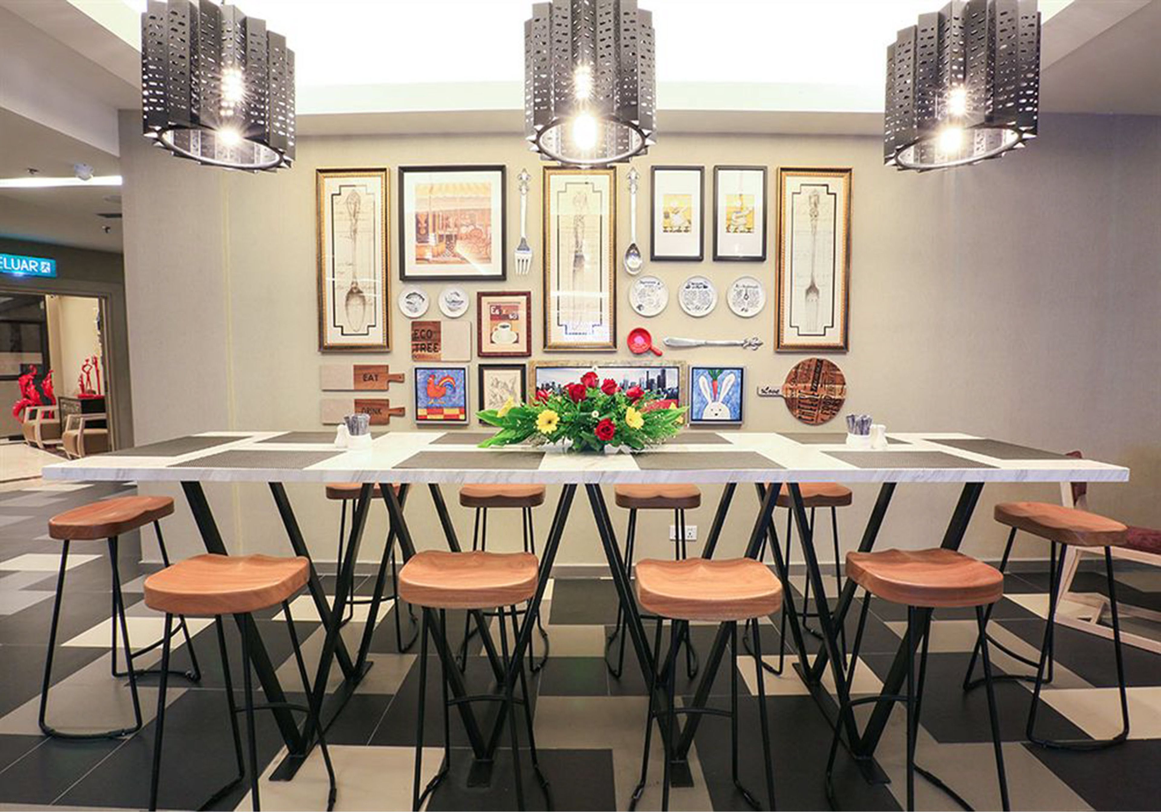 A modern dining area with a long table, multiple stools, and a variety of framed artworks on the wall.