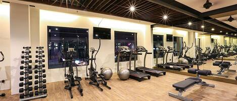 A gym with exercise equipment, mirrors, and large windows.