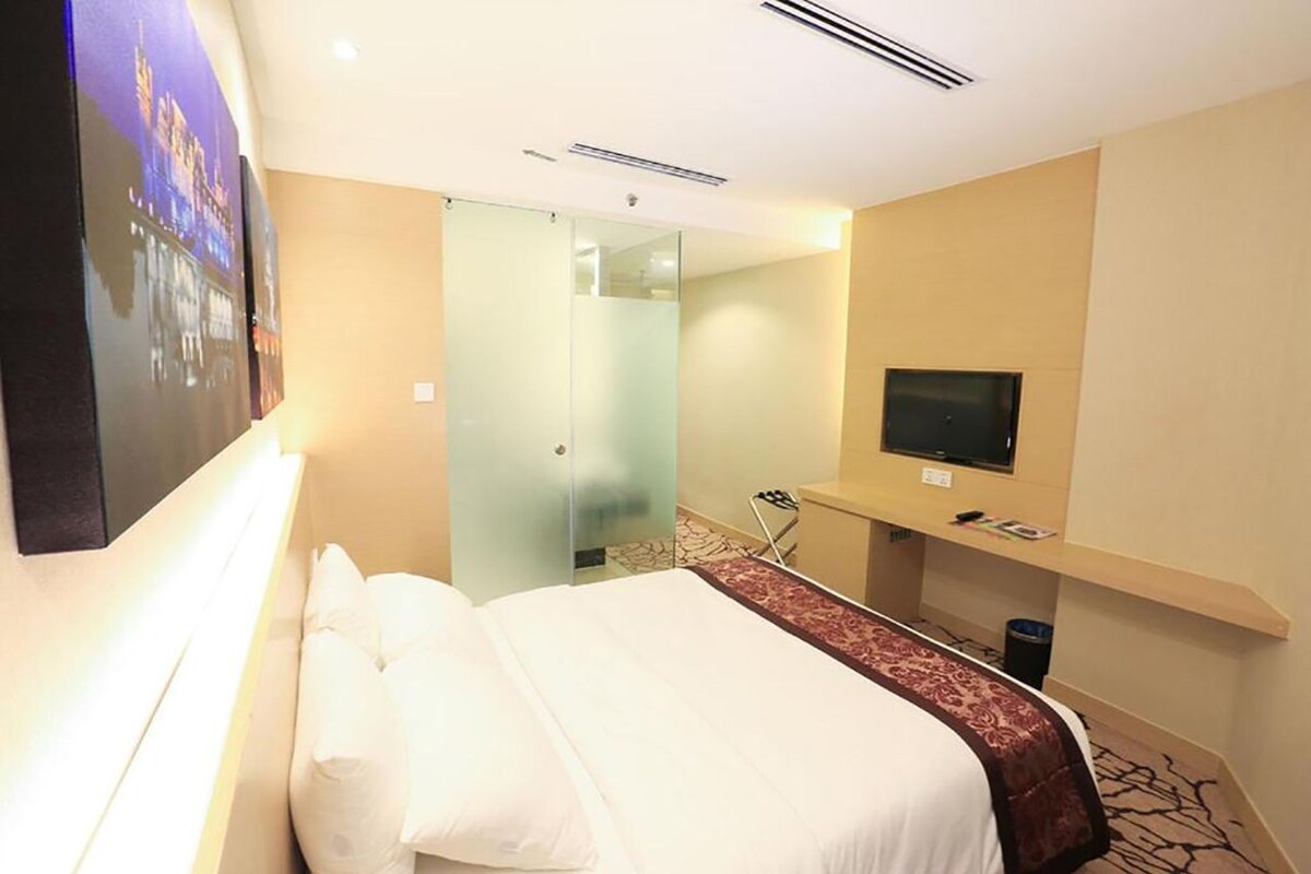A hotel room with a bed, a television, a mirror, and a glass partition.