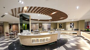 Un hall d’hôtel moderne doté d’un espace buffet central, de différents types de sièges et d’un comptoir d’enregistrement.